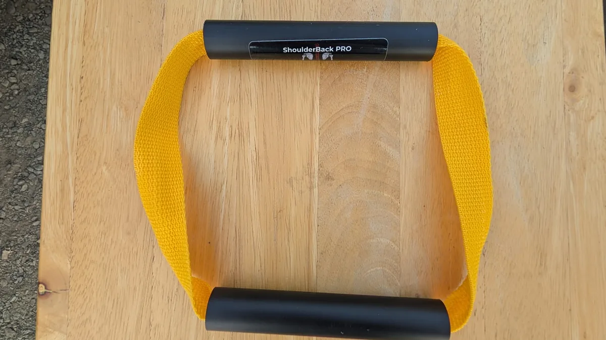 ShoulderBack Pro trainer with a yellow strap and two black handles on a light wooden table