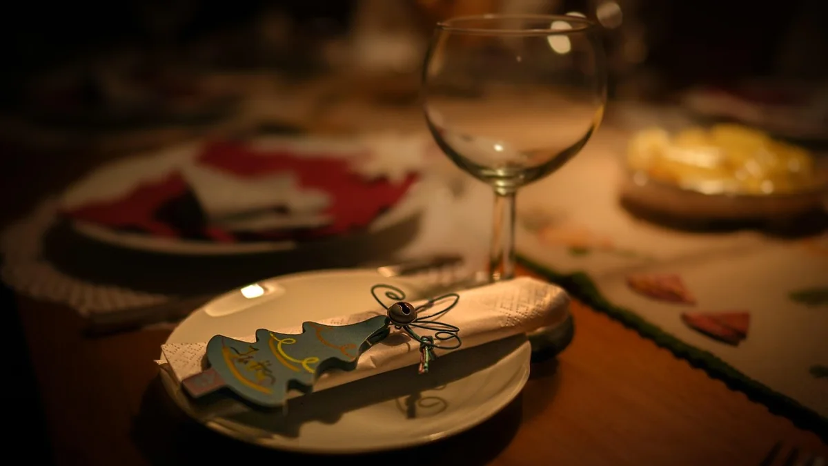 A set dining table with plates, a folded cloth napkin and a small bowl of greenery, lit by warm late-afternoon light