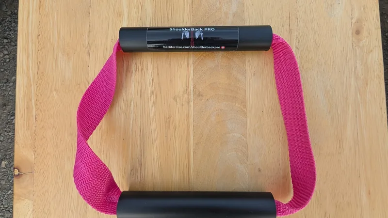ShoulderBack Pro trainer with a pink strap and two black handles on a light wooden table