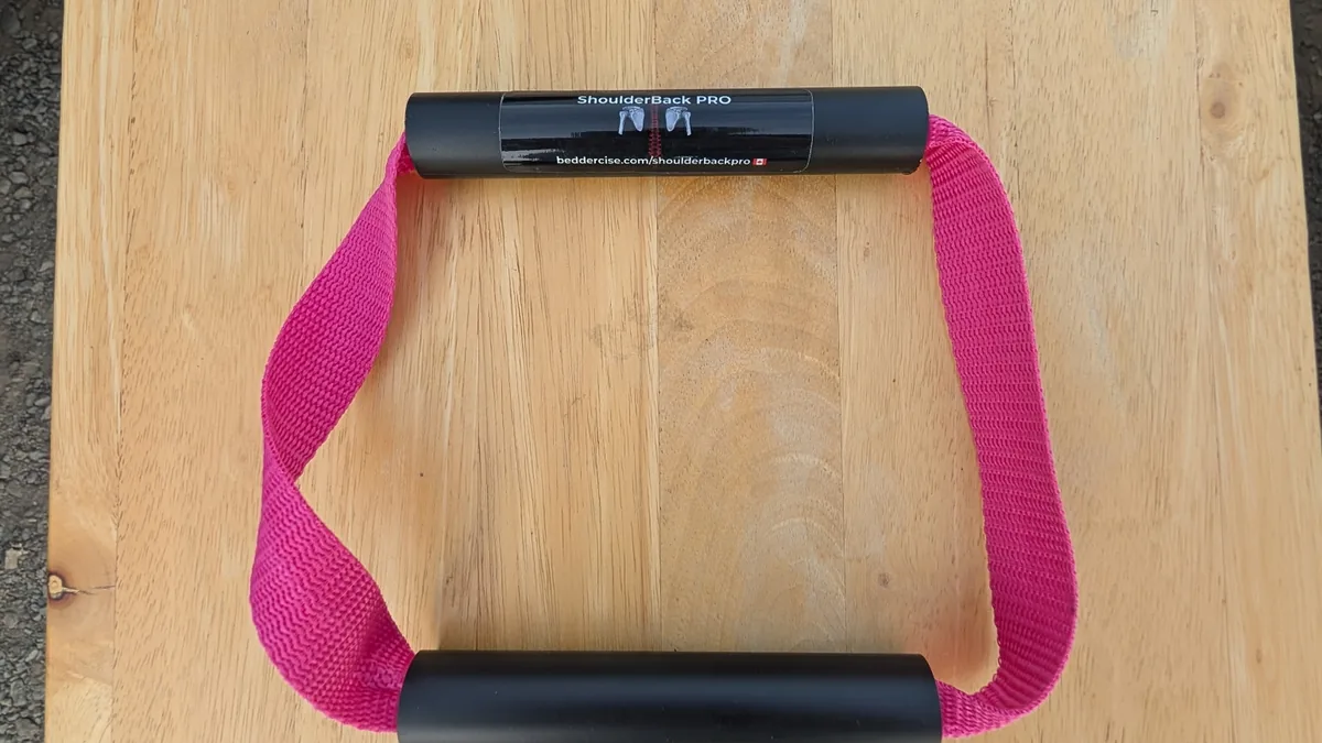 ShoulderBack Pro trainer with a pink strap and two black handles on a light wooden table