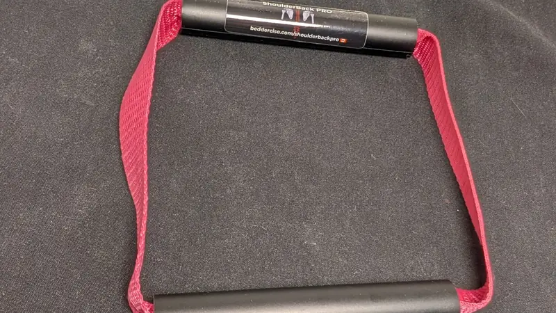 ShoulderBack Pro trainer with a burgundy strap resting on a dark cushion