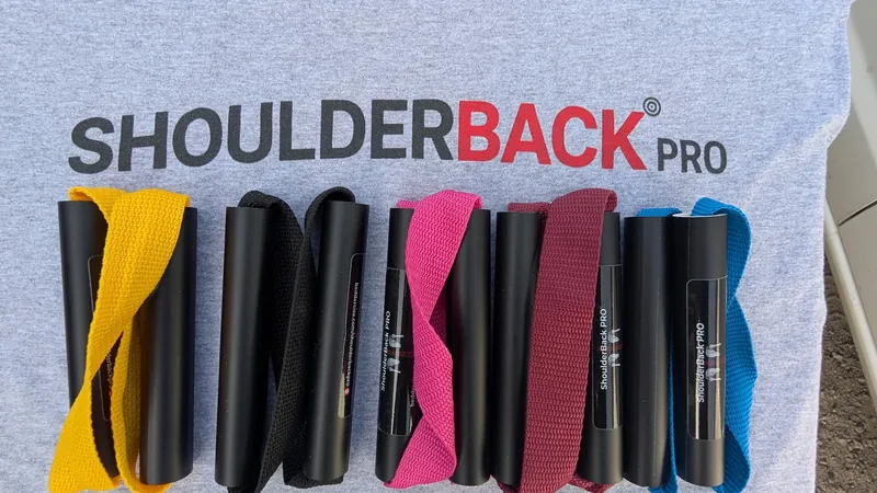 Five ShoulderBack Pro trainers in yellow, black, pink, burgundy and blue laid on a grey ShoulderBack Pro shirt