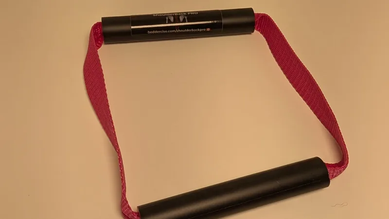 ShoulderBack Pro trainer with a pink strap on a white desk under warm indoor light