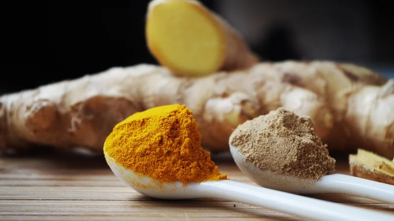 A small dish of turmeric, ginger root and a glass of water on a kitchen counter, in soft morning light
