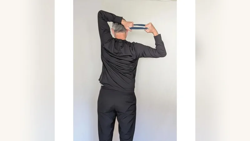 Van from behind, holding the ShoulderBack Pro trainer overhead and behind his head