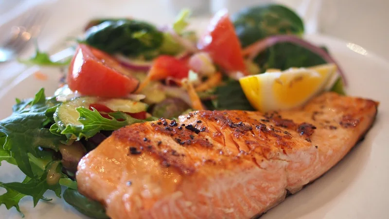 Grilled salmon fillet with lemon and green beans on a plain white plate, on a kitchen table