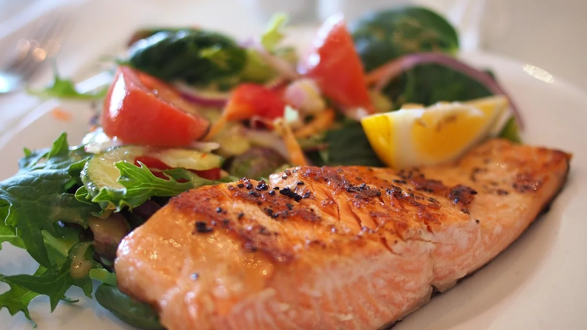Grilled salmon fillet with lemon and green beans on a plain white plate, on a kitchen table