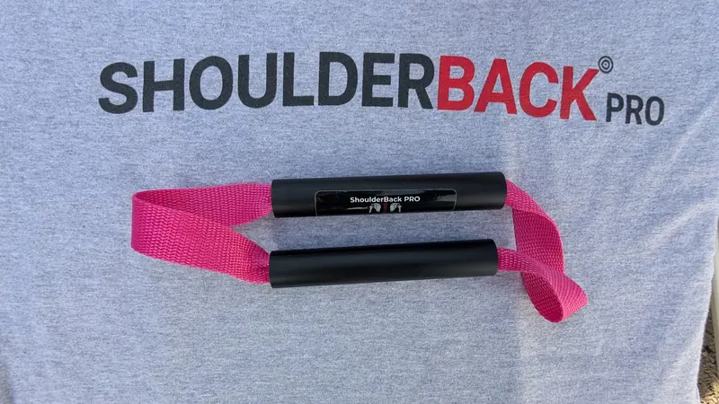 ShoulderBack Pro trainer with a pink strap resting on a grey ShoulderBack Pro shirt