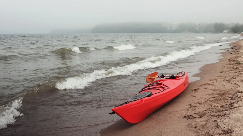 A kayak on calm water beside a grassy shore, with a paddle resting across the bow