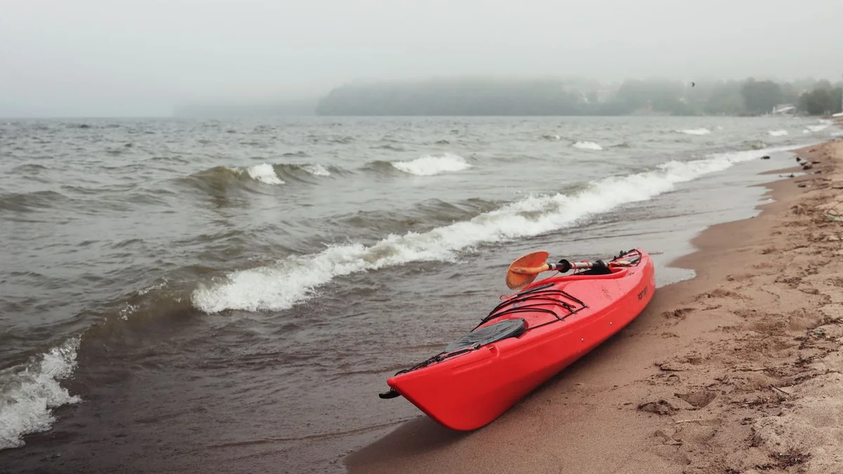 A kayak on calm water beside a grassy shore, with a paddle resting across the bow