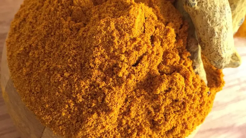 A small bowl of ground turmeric and a few whole roots on a wooden table beside a glass of water