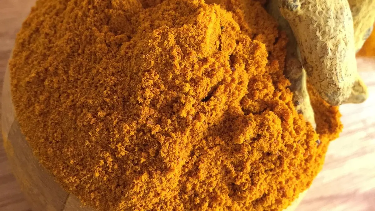 A small bowl of ground turmeric and a few whole roots on a wooden table beside a glass of water
