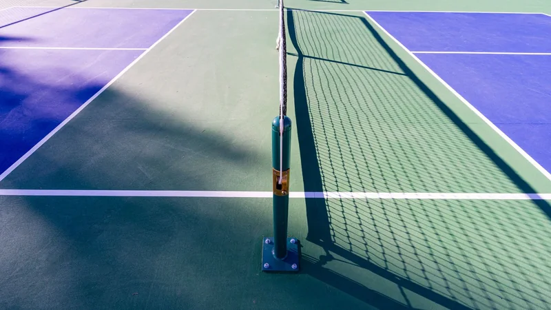 An empty outdoor pickleball court with white lines and a net in soft late-afternoon light