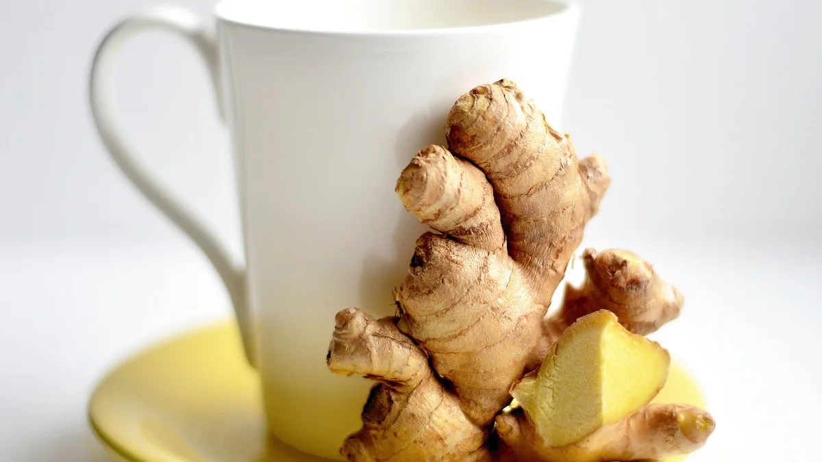 Fresh ginger root and a small cup of tea on a wooden cutting board