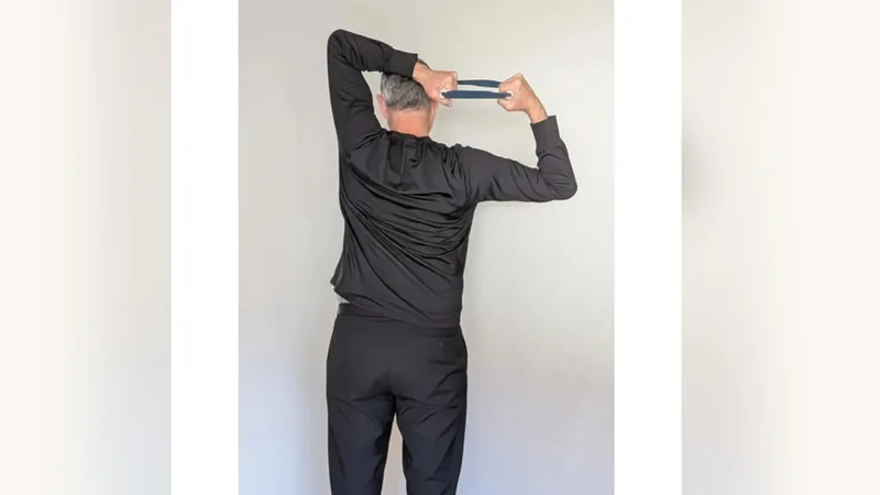 Van from behind, holding the ShoulderBack Pro trainer overhead and behind his head