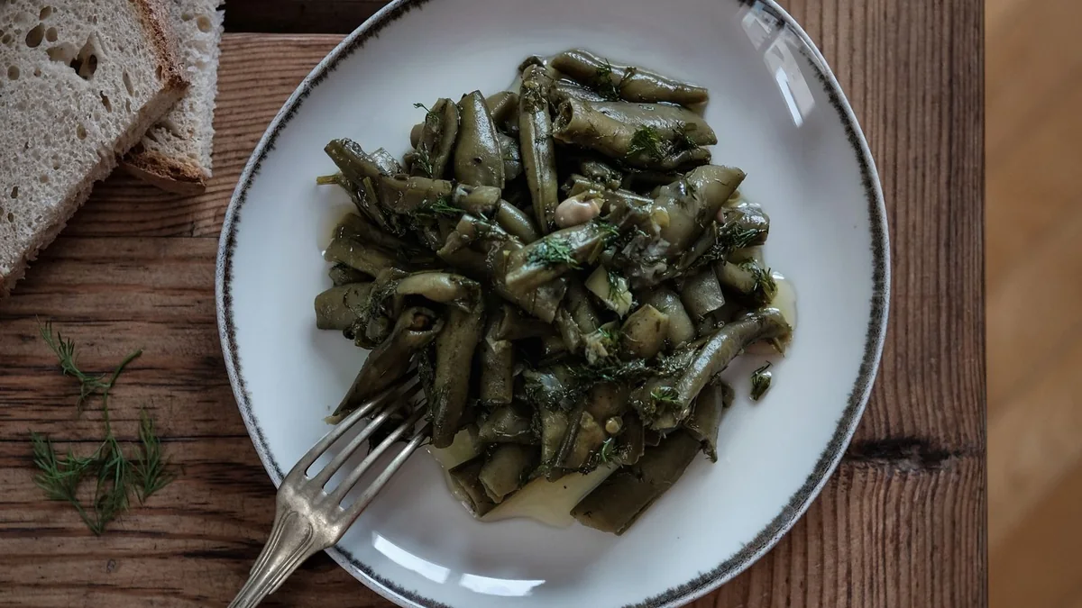 A simple meal of vegetables, beans, olive oil and bread on a table, shot from above with natural light.