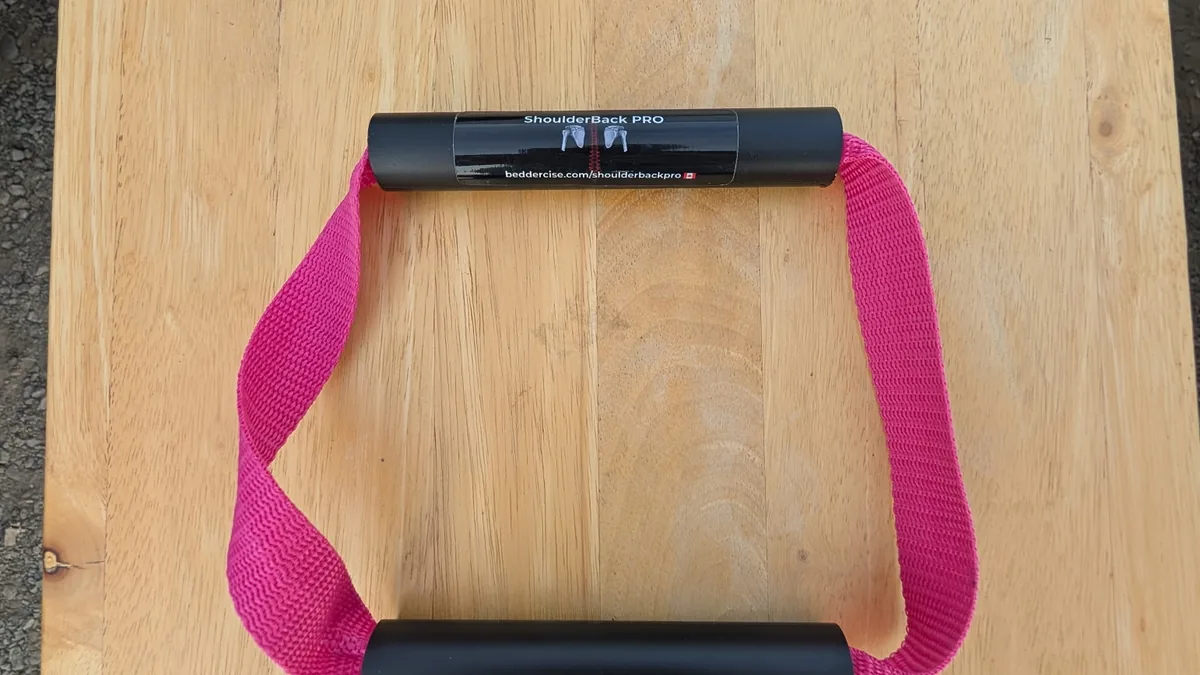 ShoulderBack Pro trainer with a pink strap and two black handles on a light wooden table