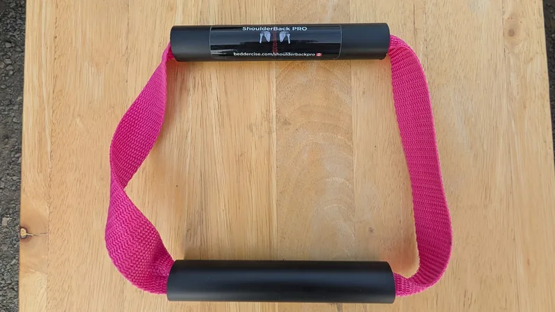 ShoulderBack Pro trainer with a pink strap and two black handles on a light wooden table
