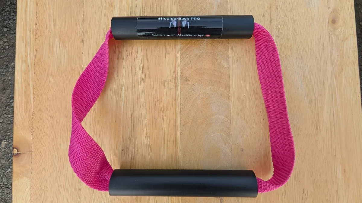 ShoulderBack Pro trainer with a pink strap and two black handles on a light wooden table
