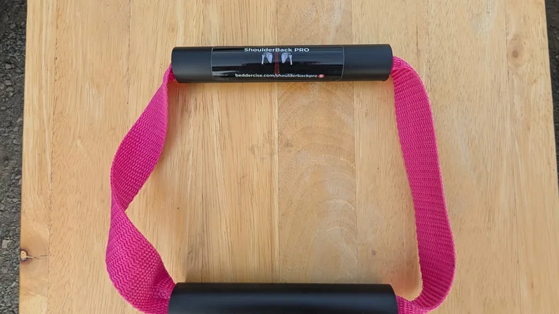 ShoulderBack Pro trainer with a pink strap and two black handles on a light wooden table