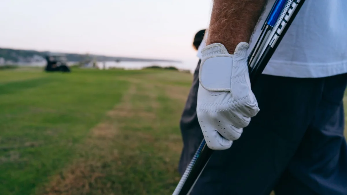 A golfer's gloved hands gripping a club on a green fairway in soft morning light