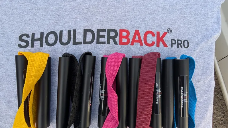 Five ShoulderBack Pro trainers in yellow, black, pink, burgundy and blue laid on a grey ShoulderBack Pro shirt