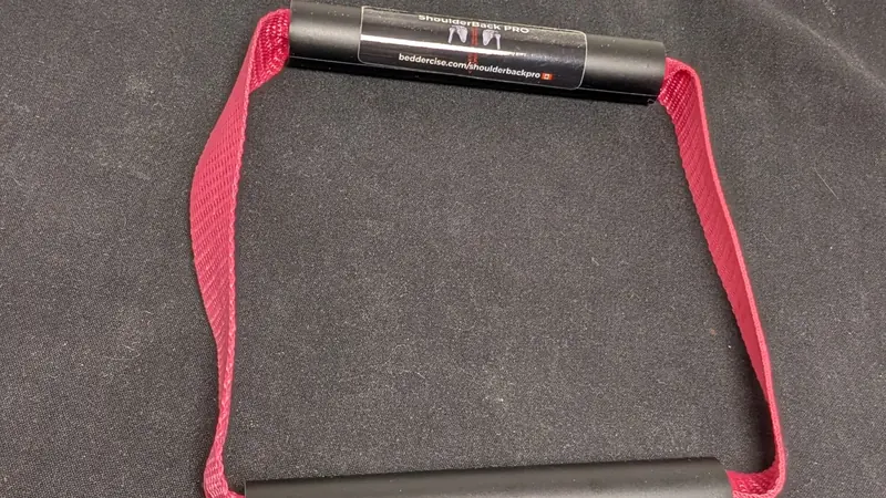 ShoulderBack Pro trainer with a burgundy strap resting on a dark cushion