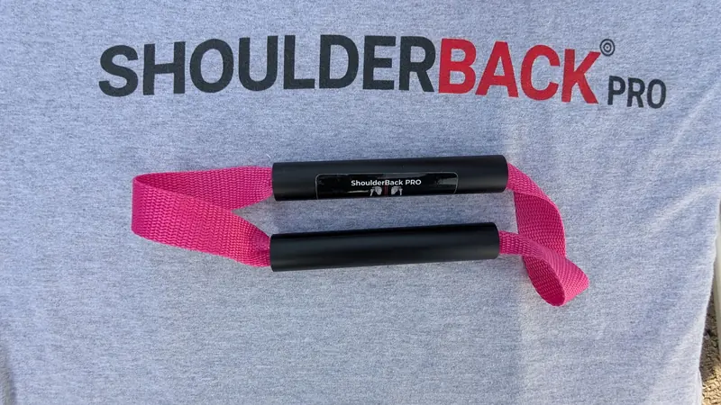 ShoulderBack Pro trainer with a pink strap resting on a grey ShoulderBack Pro shirt