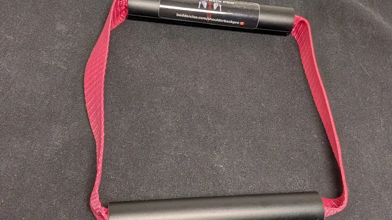 ShoulderBack Pro trainer with a burgundy strap resting on a dark cushion