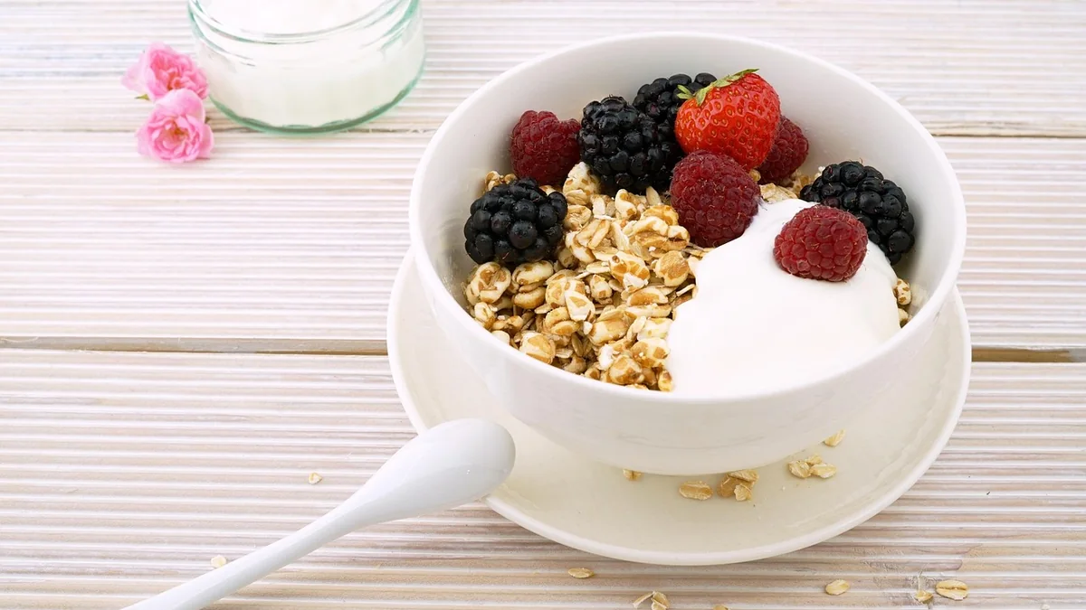 A simple bowl of Greek yogurt with berries and a spoon on a kitchen counter, with eggs in a bowl nearby