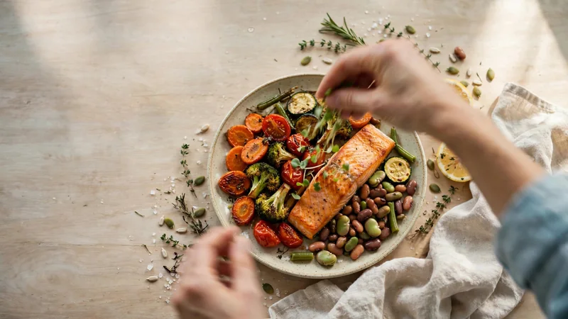 A colourful plate of roasted vegetables, beans and salmon on a wooden table, seen from above