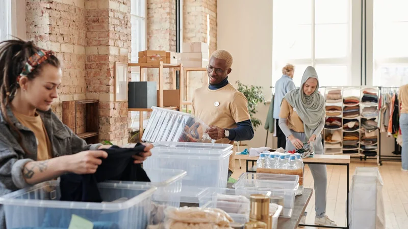 Volunteers sorting donated items at a community table in a bright room, one person seated and one standing