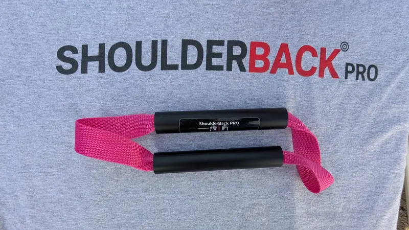 ShoulderBack Pro trainer with a pink strap resting on a grey ShoulderBack Pro shirt