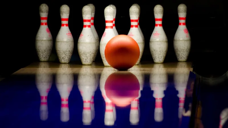 A bowling ball resting on a polished wooden lane near a row of white pins, in soft overhead light