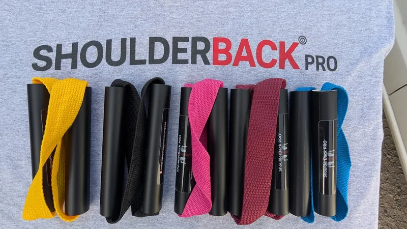 Five ShoulderBack Pro trainers in yellow, black, pink, burgundy and blue laid on a grey ShoulderBack Pro shirt