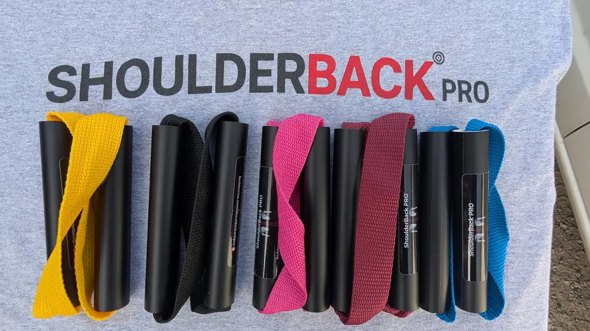 Five ShoulderBack Pro trainers in yellow, black, pink, burgundy and blue laid on a grey ShoulderBack Pro shirt