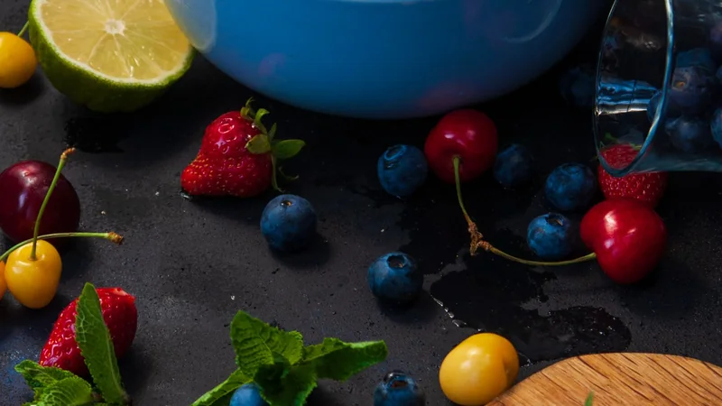 A white bowl of fresh mixed berries and a few cherries on a kitchen counter, with a glass of water beside it