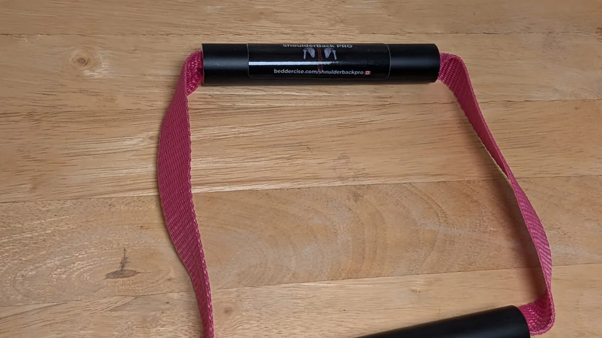 ShoulderBack Pro trainer with a pink strap on a wooden table, photographed at an angle