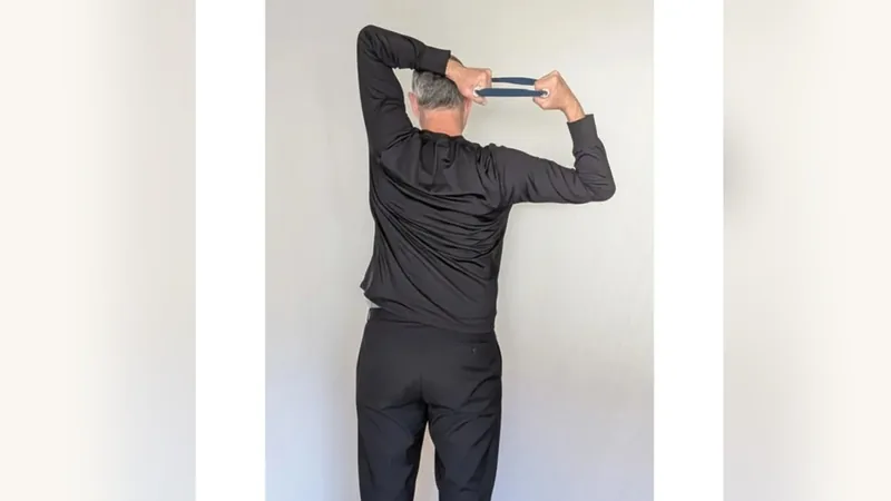 Van from behind, holding the ShoulderBack Pro trainer overhead and behind his head