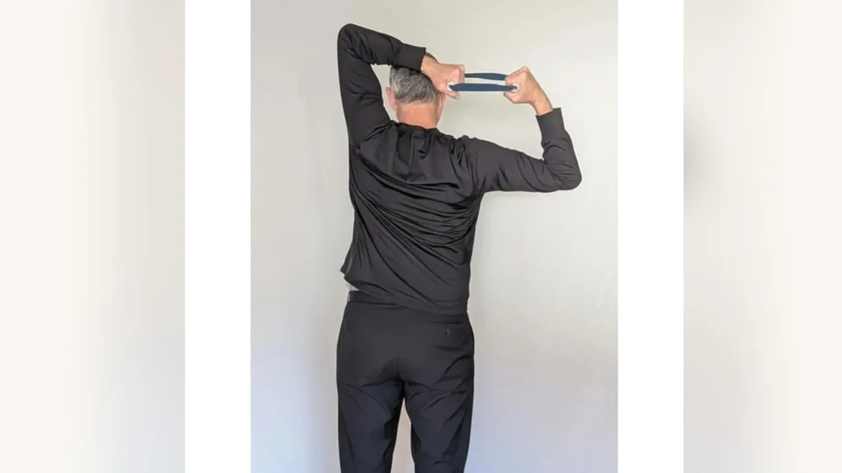 Van from behind, holding the ShoulderBack Pro trainer overhead and behind his head