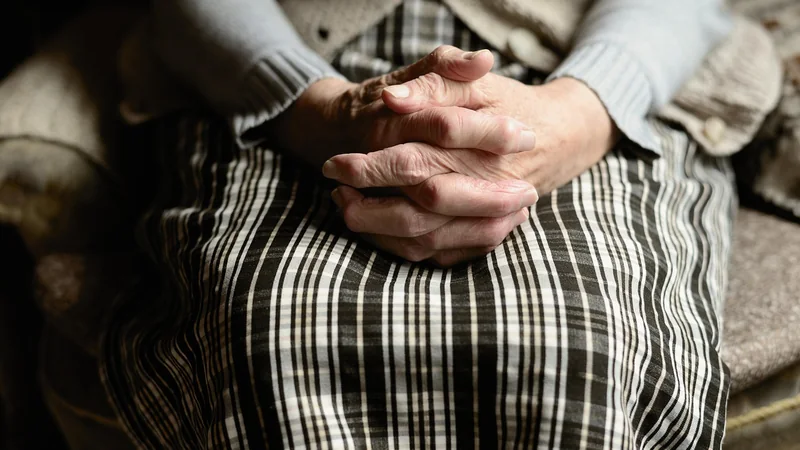 Hands resting loosely on the lap of a person sitting in a sunlit armchair, with a window in the background