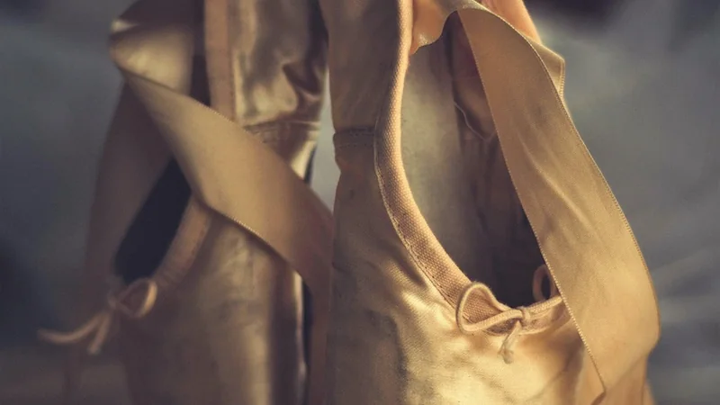 A pair of dancing shoes on a wooden floor beside a folded chair, in warm light
