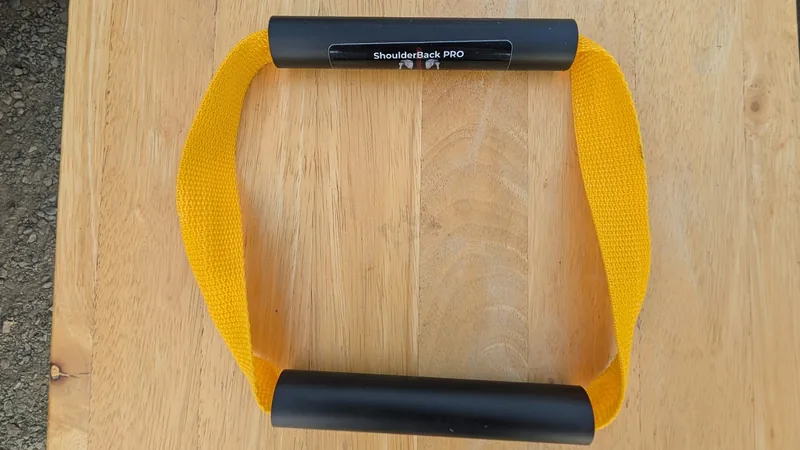 ShoulderBack Pro trainer with a yellow strap and two black handles on a light wooden table