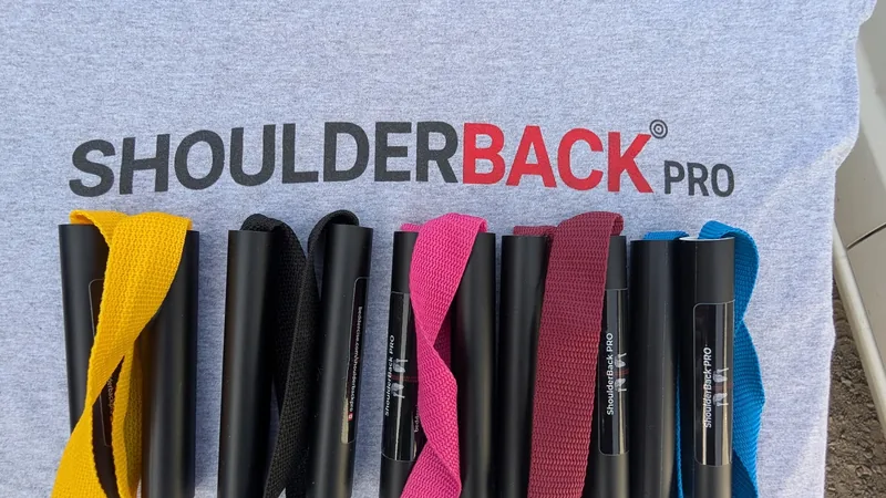 Five ShoulderBack Pro trainers in yellow, black, pink, burgundy and blue laid on a grey ShoulderBack Pro shirt