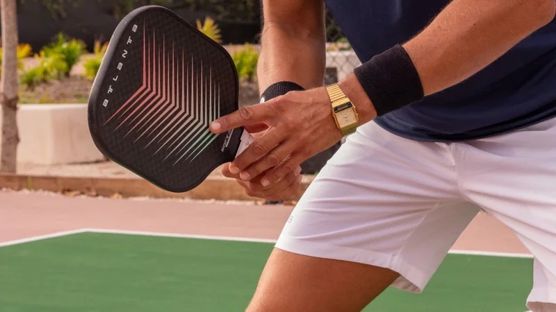 A person on an outdoor court holding a paddle at shoulder height mid-rally, in relaxed, balanced stance