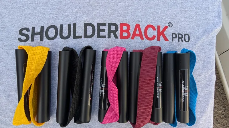 Five ShoulderBack Pro trainers in yellow, black, pink, burgundy and blue laid on a grey ShoulderBack Pro shirt
