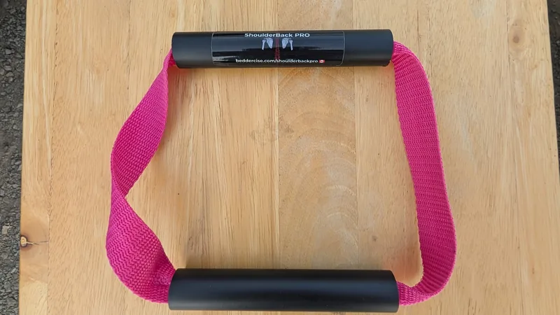 ShoulderBack Pro trainer with a pink strap and two black handles on a light wooden table