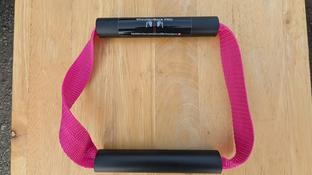ShoulderBack Pro trainer with a pink strap and two black handles on a light wooden table