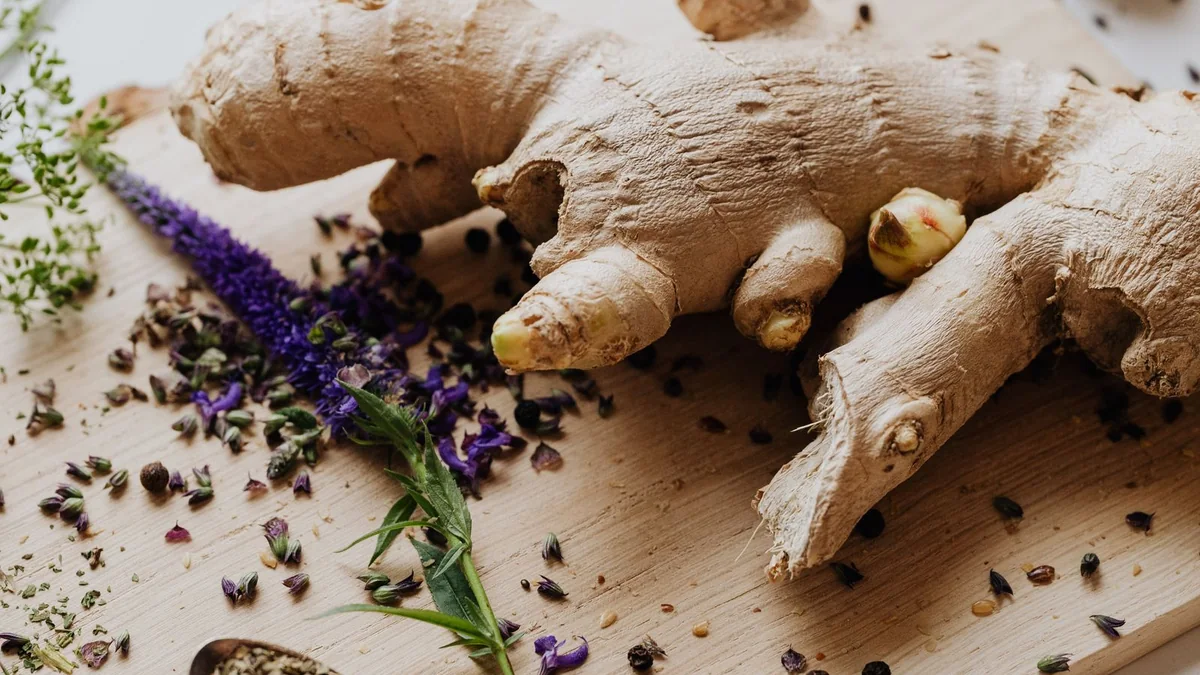 A wooden cutting board with fresh ginger root, a small pile of turmeric powder, and whole garlic bulbs, in soft daylight.