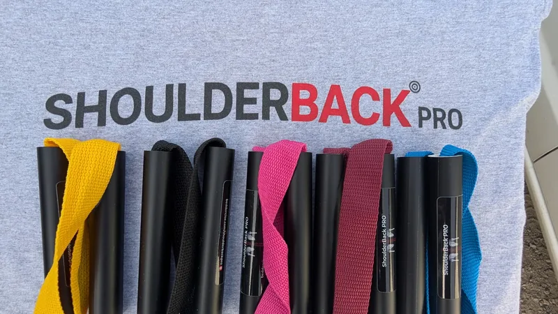 Five ShoulderBack Pro trainers in yellow, black, pink, burgundy and blue laid on a grey ShoulderBack Pro shirt